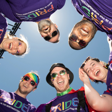 A group of six from Northwestern, wearing rainbow-colored gear, stand in a circle looking at its center and smiling