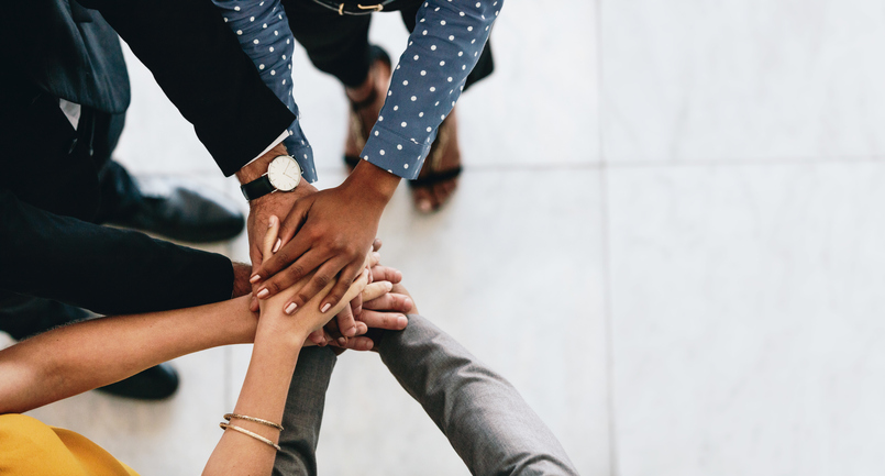 A circle of people stack their hands on top of one another.