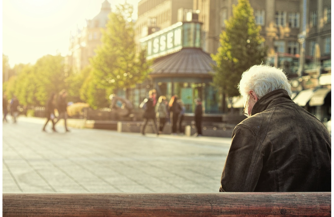 Older male sitting on bench in park with his head down 