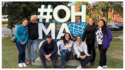 Image of a group of seven people in front a sign that reads #OH MAGOG